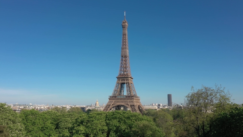France, Paris Tour Eiffel (Eiffel tower) with blue sky and green trees in the foreground. 4k quality drone shot, aerial view from bottom to top (looks like crane or drone shot) | Shutterstock HD Video #1055360339