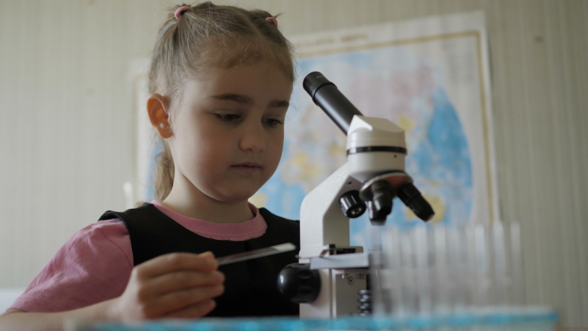 Little girl in science lab study samples under microscope. Schoolgirl looking through microscope in science class. Child looking into microscope, studing biology, chemistry in school laboratory.