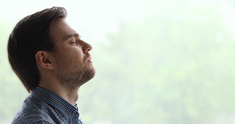 Peaceful man pose aside near window background closed eyes breath fresh air feels calm. Anxiety relief, brings internal state in order exercise, close up side view face. No stress, mindfulness concept