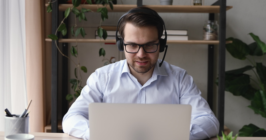 Positive businessman sit at desk wear headset looking at laptop screen enjoy informal chat talking with colleague mate laugh over anecdote, interact with company client by video conference application Royalty-Free Stock Footage #1055363189