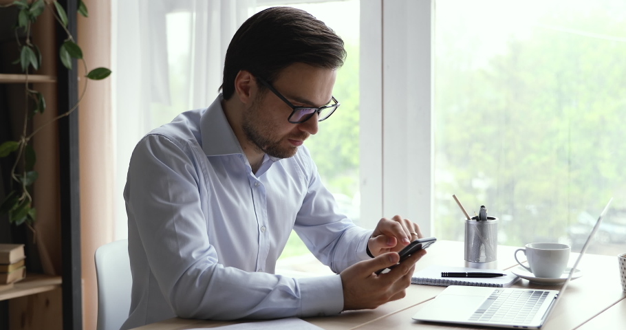 Businessman in glasses sit at desk receive sms feels happy celebrating moment of victory. Career promotion, salary increase bank notification, bet auction bid monetary win, sincere reaction of success Royalty-Free Stock Footage #1055363204