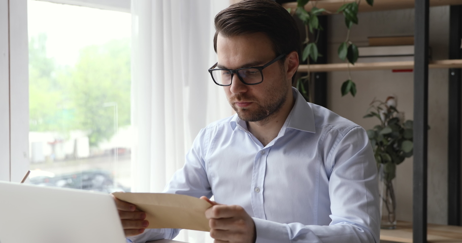 Businessman sitting at workplace desk open envelope take out letter reads it feels happy. Career growth advance promotion, bank loan approve, monetary award, long-awaited invitation great news concept Royalty-Free Stock Footage #1055363222
