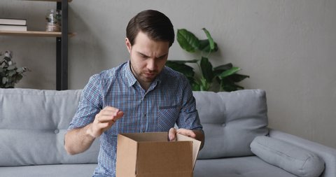 Man sitting on couch unpack received delivered parcel small box feels mad and frustrated due fragile goods broken, wrong order, bad condition or low-quality dissatisfied online purchase client concept