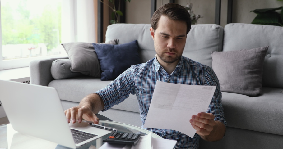 Man working from home holding invoice using calculator and laptop calculates costs, makes payments through e-bank application. Business or household expenses, manage budget incomes or outcomes concept Royalty-Free Stock Footage #1055363333