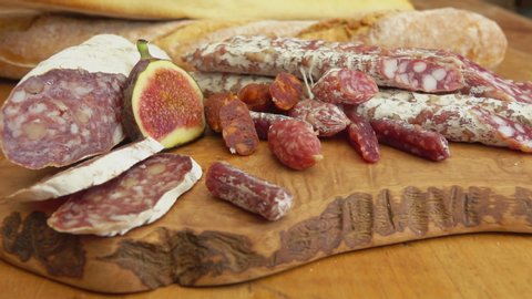 Panorama of delicious dry sausages laying on a wooden board with figs and baguettes
