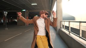 Cheerful and happy young man with beard actively dancing while walking down the street on sunset background. He's wearing a brown jacket. Urban concrete park next to business center. Sunny. - Powered by Shutterstock - Get 15% off with code: PIKWIZARD15