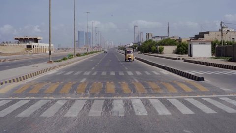Karachi, Pakistan - 2020: Speed bump painted with yellow color for safety while a white Toyota car comes towards the camera on the main sea view road. Dolmen Mall and Bahria Icon Tower kisses the sky.