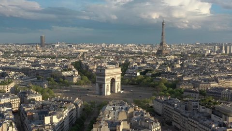 France, Paris Arc de Triomphe (Triumphal Arch) in Champs Elysees and Eiffel tower behind, at sunset (or sunrise). 4k Quality shot, forward drone shot, aerial view