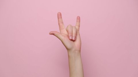Rock-n-roll concept. Close up female hand waving with horns gesture, isolated on pink studio background with copy space for advertisement. With place for text or image. Body language