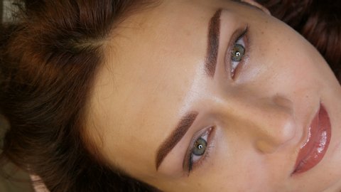 Beautiful young woman with permanent lip make-up and microblading eyebrow tattoo lies with a beauty parlor after the procedure. Close-up girl face.