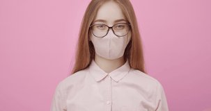 Portrait of attractive woman with blond hair in medical mask shaking her head to express negative reaction over pink background. Concept of real human emotions.