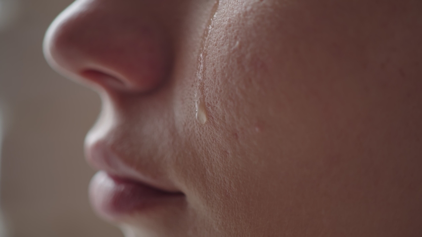 Close-up of a woman's cheek with a tear sliding down it. A tear slowly descends on the distressed face of a young girl, macro Royalty-Free Stock Footage #1055375570