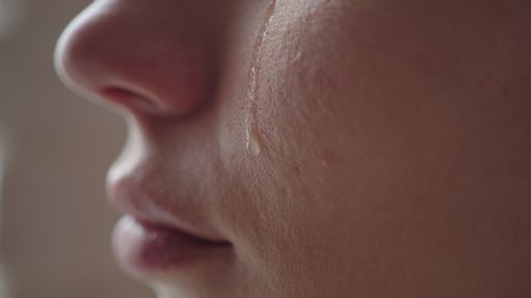 Close-up of a woman's cheek with a tear sliding down it. A tear slowly descends on the distressed face of a young girl, macro