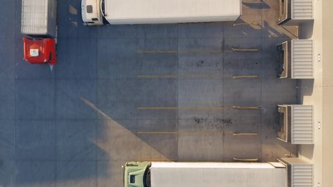 Aerial top down view of a lot of semi trucks with cargo trailers awaiting for loading/unloading goods on ramps on the big logistics park with loading hub and warehouse