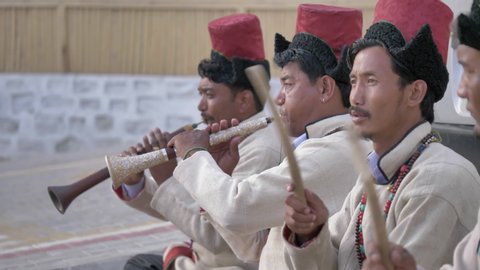 Ladakhi folk musicians men/ males in traditional costumes playing musical instruments outdoors in a Tibetan village, Leh, Ladakh, India (March 2020)