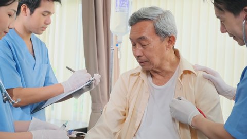 Asian medical team doctors nurse examining and checking Asian elderly male patient, health care staff take note on clipboard and pressure check with conversation in hospital. 