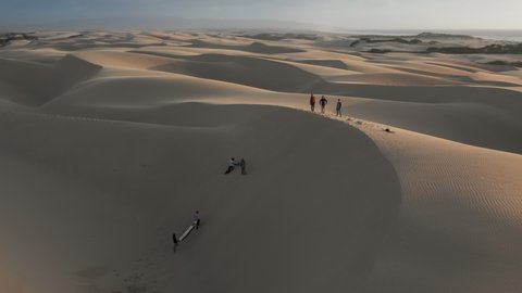 Aerial slow motion video of a people in the desert at sunset. Group of travelers in colorful sports wear is relaxing on the top of golden ripples sand dunes. 4K California nature landscape