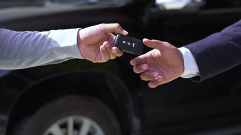 Car salesman finishing up dealing car and shaking hands. Businessman giving car key contract buying black car in vehicle showroom gallery. slow motion shot.