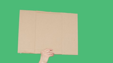 Empty cardboard human hand holding on green chromakey screen background. Unrecognizable men showing cardboard banner at empty green screen