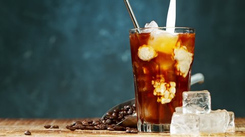 Slow motion pouring cold brew iced coffee into a glass over ice cubes