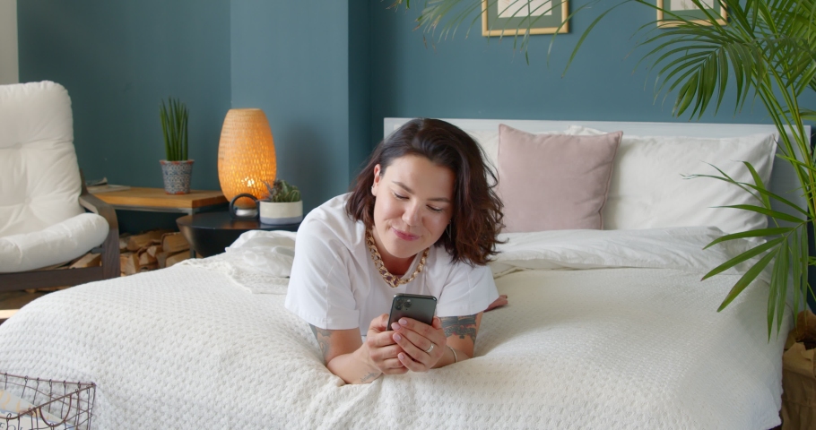 Young single woman using dating app on her phone, swiping and touching screen, at home lying on bed. Female using smart phone surfing social media, checking news, playing mobile games, texting message Royalty-Free Stock Footage #1055394857
