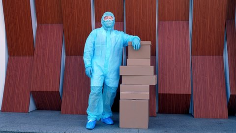 Delivery of parcels with medical equipment or drugs to hospital during coronavirus outbreak. Courier, in protective uniform, goggles, standing near stack of cardboard boxes. Cargo delivery service