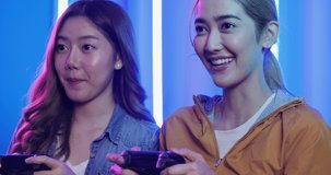Asian woman gamer playing console game together with funny emotion. Gamer female controlling joysticks and fighting together in console video game.