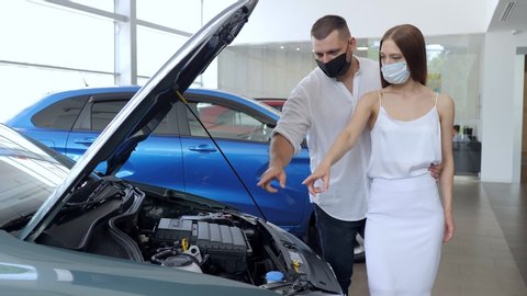 Couple in a car salon. European couple in protective masks buying the car during the quarantine