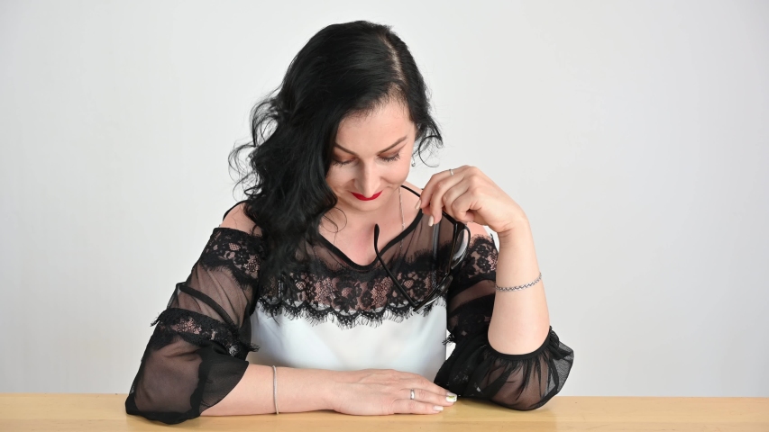 Business woman in a blouse laughs merrily while sitting at a table. Portrait of a caucasian model with curly black wavy hair on a white background in studio.