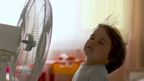 Boy Standing in Front of Fan. Child Enjoying Cool Wind From Electric Fan at Home at Summer Vacation. Suffer From Heat High Temperature in Front of Ventilator Cooling Herself With Electric Fan-Cooler.