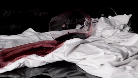 A full glass of wine falls over a tablecloth and the liquid sucks into the material. On black background.