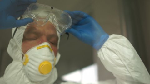 Doctor during a coronavirus pandemic covid-19 takes off glasses and a protective mask, face marks are visible from the mask, red spots. Close portrait of a tired doctor behind the glass