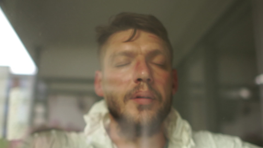 Close portrait of a tired doctor in a protective suit behind a protective glass in a hospital ward. Red prints from the mask are visible on the face. Medicine during the epidemic of coronavirus Royalty-Free Stock Footage #1055404661