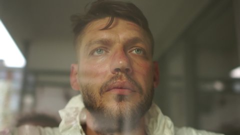 Close portrait of a tired doctor in a protective suit behind a protective glass in a hospital ward. Red prints from the mask are visible on the face. Medicine during the epidemic of coronavirus