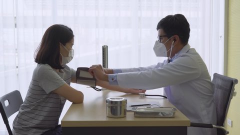 doctor using manual sphygmomanometer to measure blood pressure of asian patient who has hypertension at the clinic in hospital. healthcare and medical concept