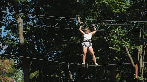 Teen girl overcomes obstacles between trees at a height. Rope town. Summer Leisure and Vacation Concept.