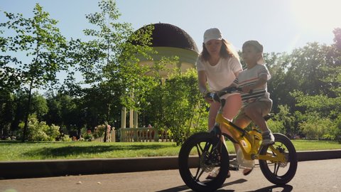 Mom teaches her little son to ride a bicycle in the city park, slow-motion. Happy family moments. Time together mother and son.