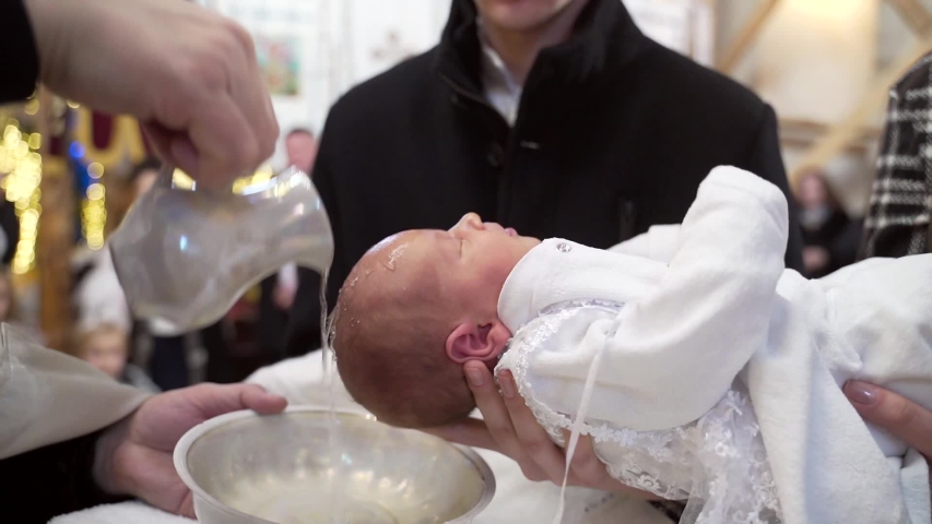 Newborn baby baptism in Holy water. Baptism in the font. Sacrament of baptism. Child and God. Christening candle Holy water font. The priest baptize. in the church | Shutterstock HD Video #1055407133