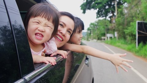 Asian family having relax vacation on holiday together. Mother and children sit and playing on back rear seat open car window to face air outside. Young daughters and mom feeling happy with smile face