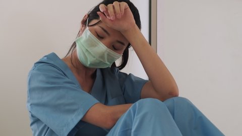 Medical team nurse feeling tired and sad from working to cure patients during covid 19 pandemic. Young woman take a break sitting close her eyes and rest after hard work at emergency case in hospital.