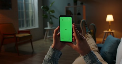 Close up shot of guy lying on couch at night, holding a smartphone with chroma key mock up green screen - technology, connections, communications concept 4k video template
