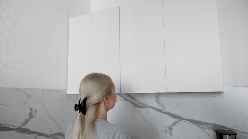 Woman open kitchenware drying rack with plates and cups in white kitchen cabinet