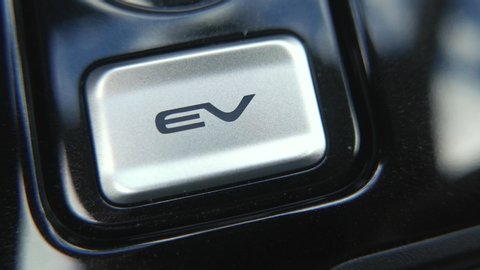 Pressing the EV button inside an electric car to activate the electric motor of the vehicle.