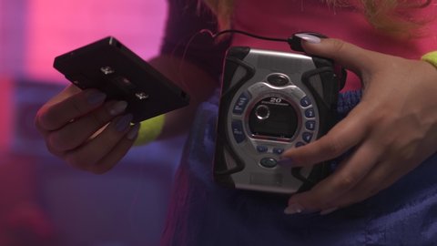 Closeup on a girl using a vintage portable cassette tape player by inserting a tape and pressing the play button to listen to her music in the 1980 1990