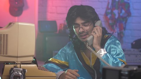 Cheesy looking young man from the 80s 90s taking a call on a land phone. Vintage background and clothing simulating the 1980 1990 era.