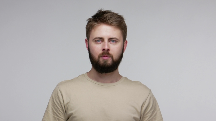 Young bearded man taking off mask, changing fake personalities, showing different facial expressions of happiness sadness rage amazement, various funny grimaces. studio shot isolated gray background | Shutterstock HD Video #1055413760