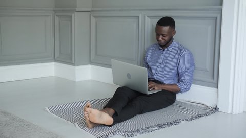 a young African-American student works on a laptop at home sitting on the floor. work or study at home