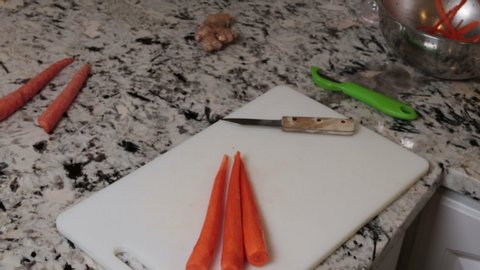 Organic orange carrots sliced into pieces by male hands with a small knife. Three carrots being cut into small pieces with a paring knife by male hands on a plastic white cutting board in a kitchen.