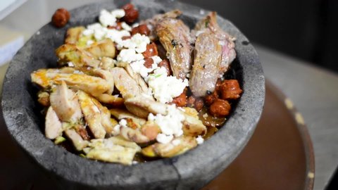  Preparing a mixed molcajete, three different meats, chicken, beef and sausage, fresh cheese and roasted tomatoes with garlic and chili served in volcanic stone. Mexican food.