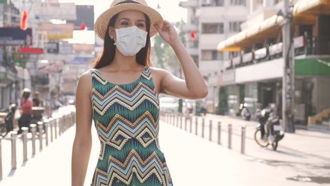 Young brunette woman traveling in Bangkok, Thailand in popular Khao San Road during pandemic Coronavirus. 20s Hispanic in a protective mask wear summer sleeveless summer dress in Asia.
